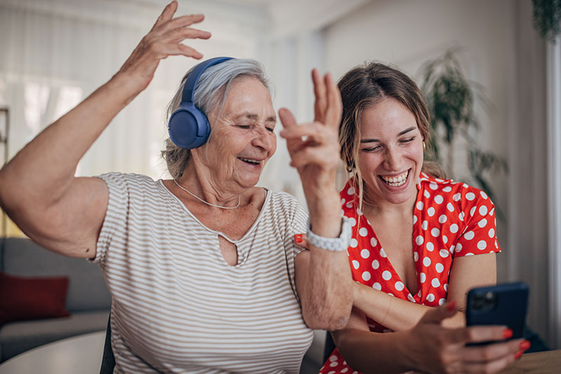 A woman caring for a loved one with dementia plays music for them both to enjoy with headphones.