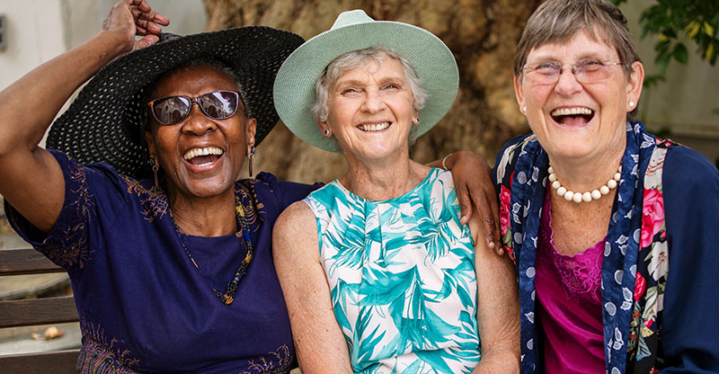 Three older women who have an optimistic outlook on aging share a laugh.
