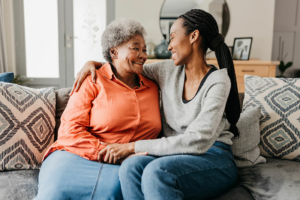 A woman who knows how important it is to empower aging parents hugs her mom on the sofa as they smile at each other.