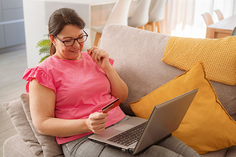 A woman smiles as she makes an online purchase on her laptop for some of the best senior care products.