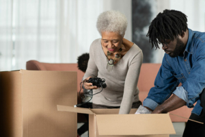 A man who knows the importance of decluttering with your parents packs items into large cardboard boxes with his elderly mother.