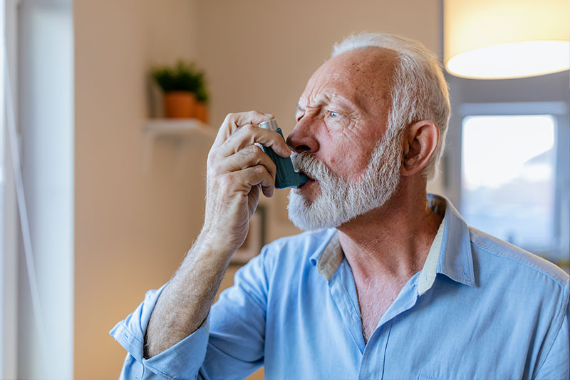 An older man experiencing COPD comorbidities uses an inhaler.