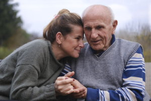 An older man struggling with Parkinson’s non-movement symptoms holds the hand of his caregiver as she leans in to give him a hug.