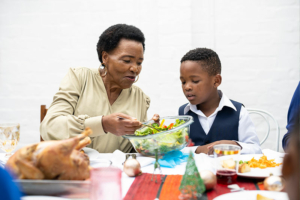 An older woman hands a plate of holiday food to her family member, as she focuses on holiday heart health for seniors.