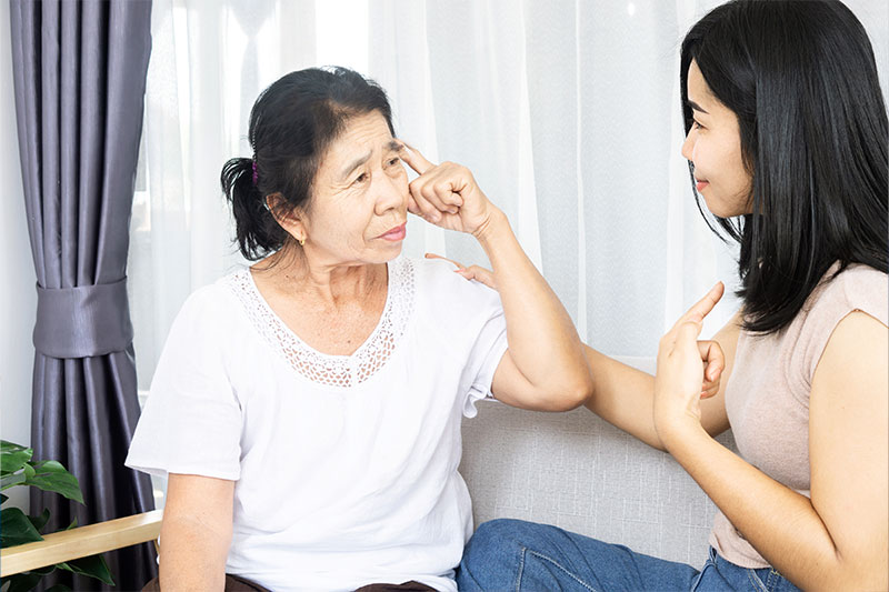 A young woman talks with an older woman who looks confused, as she navigates the emotional challenges of dementia caregiving.