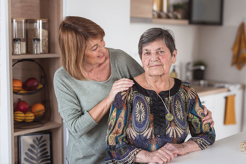 A woman who is trying to understand the way someone with dementia experiences the world places her hand on her mother’s shoulder.