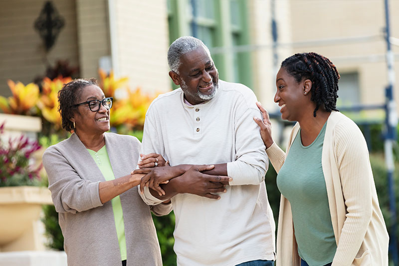 A woman supporting two elderly parents goes for a walk with them.