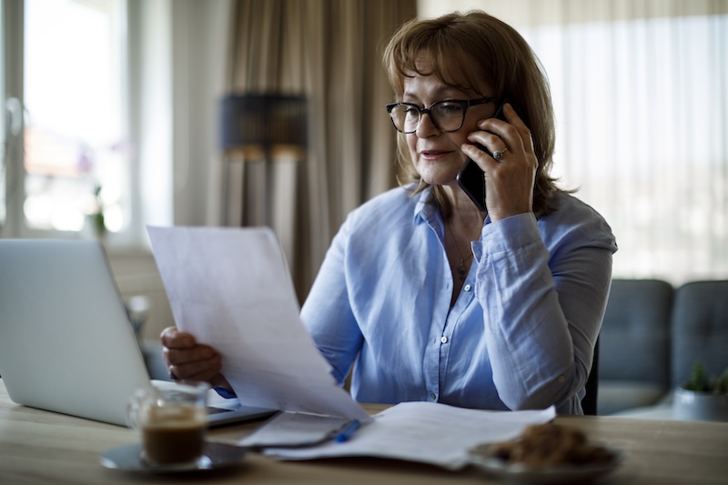 A woman reads through questions from her caregiver checklist while talking on the phone with a potential home care provider.