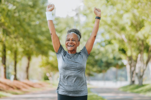 An older woman stands in the park with her arms lifted in triumph after mastering goal setting for older adults.