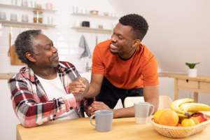 An older man who has learned how to thrive with a chronic health condition grasps the hand of his son as they smile at each other.