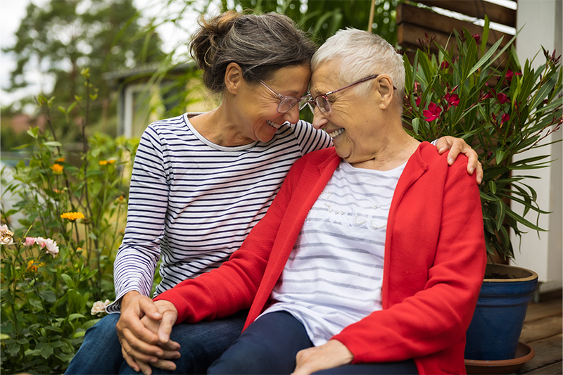 A caregiver trying to communicate with someone with Alzheimer’s wraps an arm around a smiling older woman.