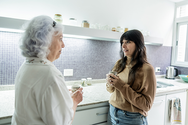 A woman who has discovered how to end disagreements with an aging parent shares a cup of coffee with her mom in the kitchen.