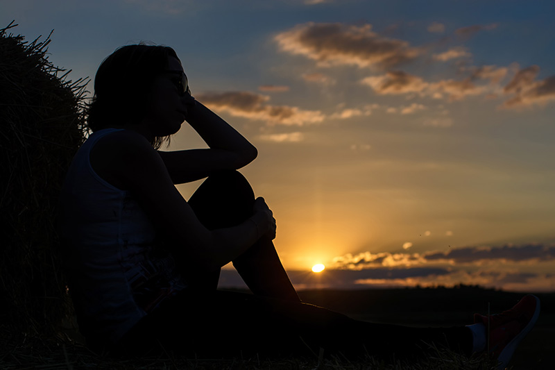 The silhouette of a woman gazing at the sunset symbolizes caregiver grief after loss.
