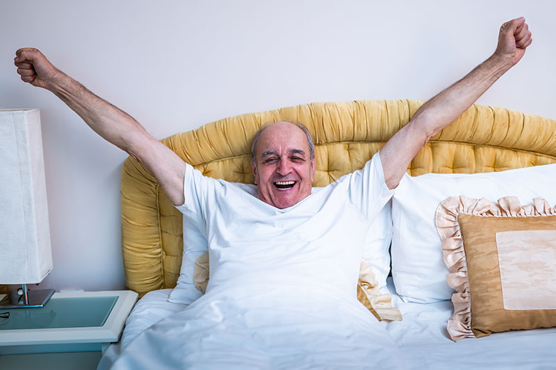 A man who knows how to get a good night’s sleep for seniors stretches and looks refreshed.