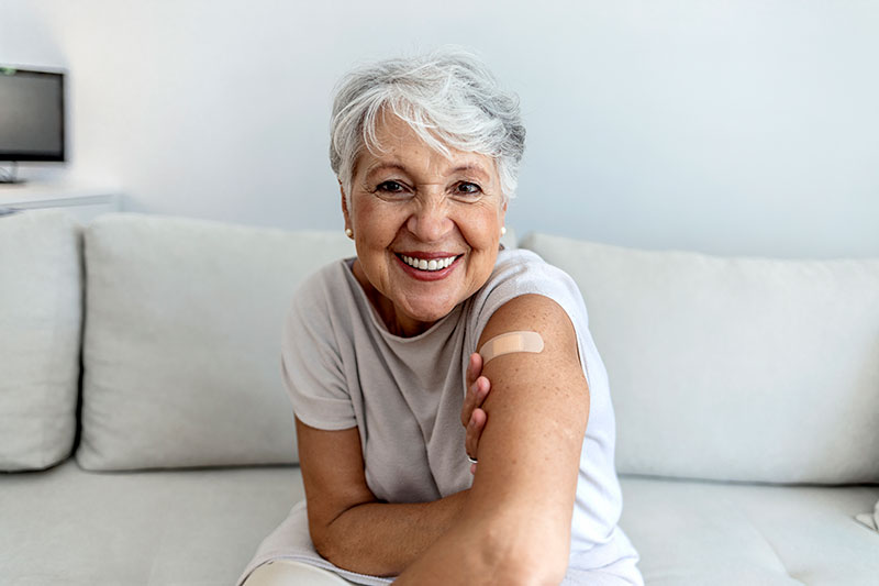 A woman receiving treatment for Alzheimer’s at home smiles as she relaxes on her sofa after her injection.
