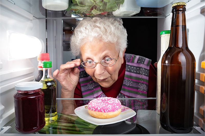 An older woman excitedly stares at a donut in her refrigerator, highlighting the signs of food addiction in seniors.