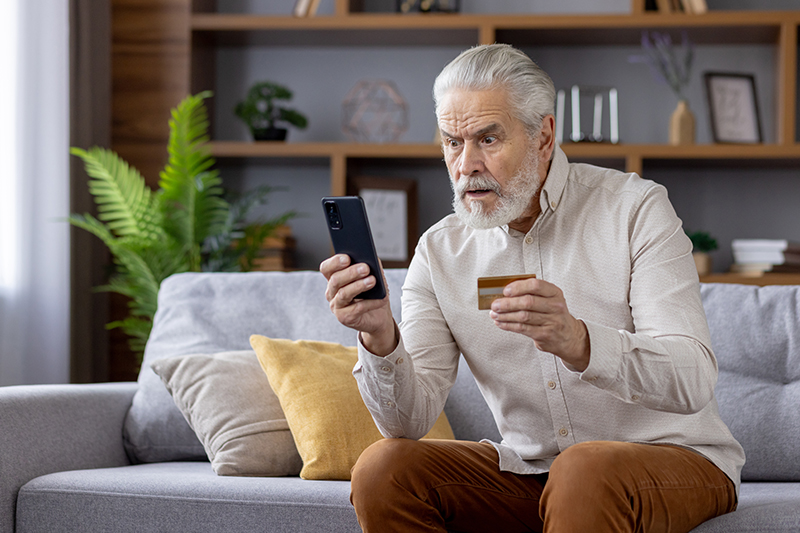 An older man stares at his phone concerned that he may have fallen victim to a scam that compromises online safety for seniors.
