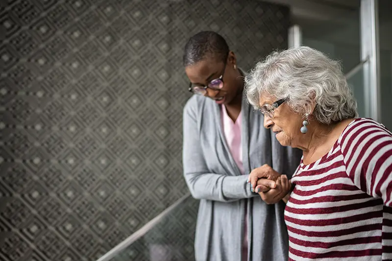A caregiver who noticed some early dementia behaviors in her client helps her navigate the stairs in her home.