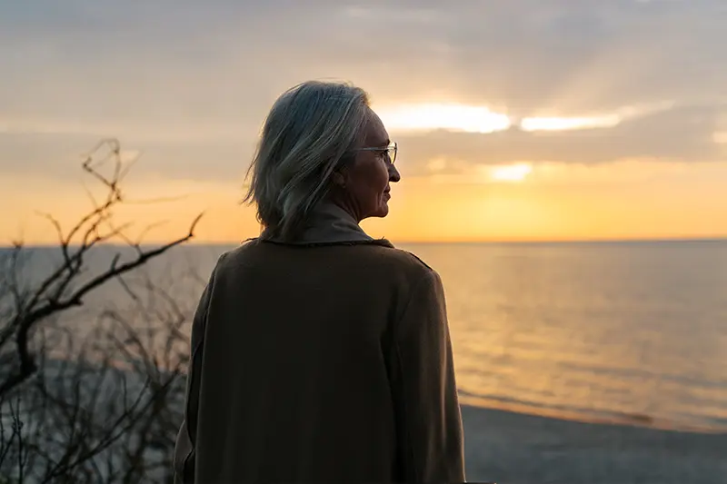 A woman contemplates the mental health needs of older caregivers as she walks along the beach.